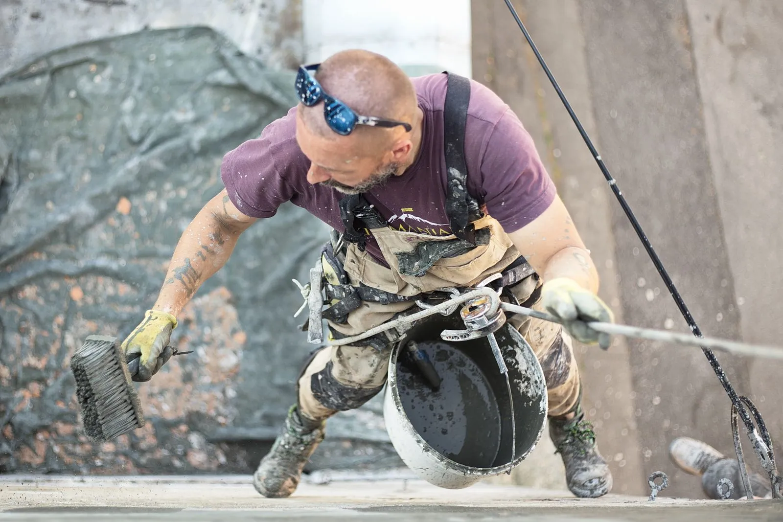 Façadier en corde qui travaille sur un mur, seau et brosse en main